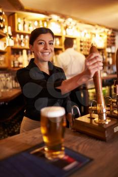 A young woman working behind a bar looking to camera