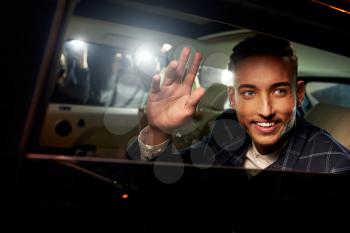 Young man waving from the back of a chauffeur driven limo
