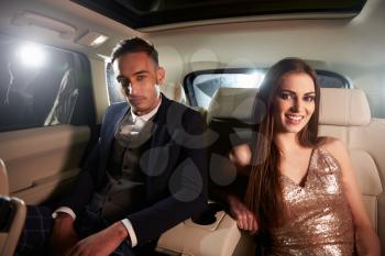 Attractive young couple in the back of a limo look to camera