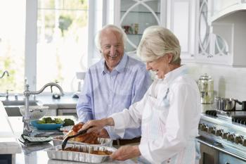 Senior Couple Make Roast Turkey Meal In Kitchen Together