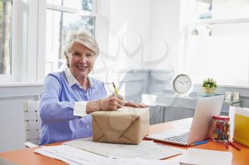 Senior Woman At Home Addressing Package For Mailing