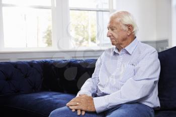 Depressed Senior Man Sitting On Sofa At Home