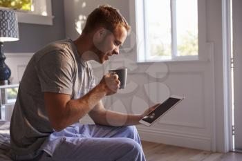 Man Wearing Pajamas Using Digital Tablet In Bedroom