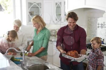 Family With Grandparents Make Roast Turkey Meal In Kitchen