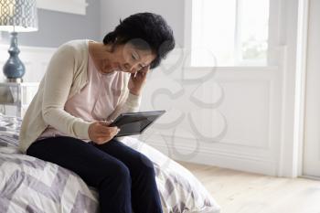 Unhappy Senior Woman Sitting On Bed Looking At Photo Frame