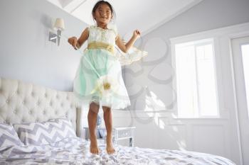 Girl Dressed In Fairy Costume Jumping On Bed At Home