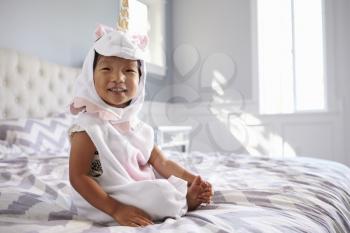Girl Dressed In Unicorn Costume Sitting On Bed At Home