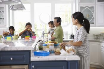 Family Having Breakfast And Making Lunches In Kitchen