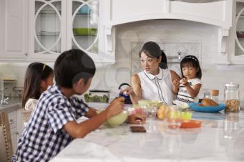 Busy Mother Organizing Children At Breakfast In Kitchen