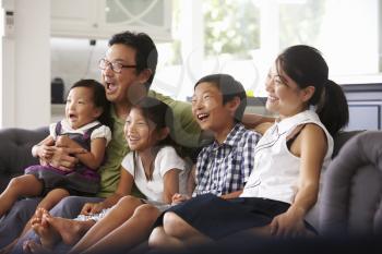 Family Sitting On Sofa At Home Watching TV Together