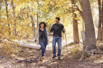 Smiling Hispanic couple walk in a forest holding hands