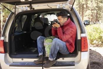 Man sitting in the open back of car taking photos in forest