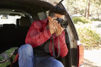 Man sitting in the open back of car taking photos, close up