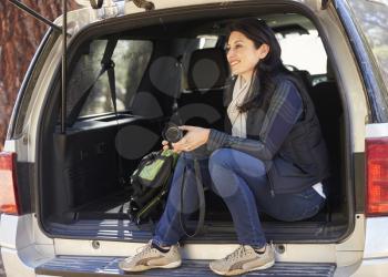 Woman holding camera sits in the open back of a car