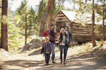 Family walking away from a log cabin in a forest