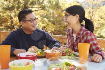 Asian couple having lunch at a table outdoors laugh together