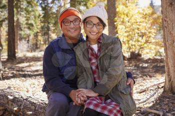 Happy Asian couple sitting in a forest looking to camera