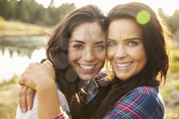 Lesbian couple hugging by a lake look to camera, close up