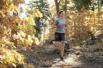 Caucasian man running on a forest trail, closer in