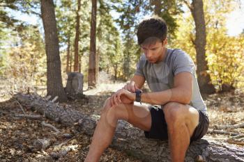 Male runner in a forest sits and checks his smartwatch
