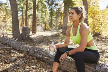 Female runner in a forest holding water bottle takes a break