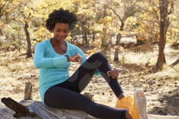 Black female runner sitting in a forest checking smartwatch