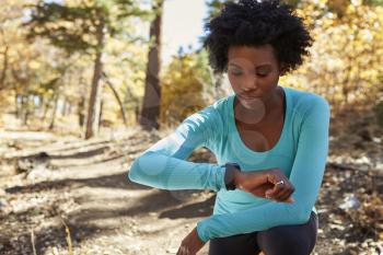 Young black woman kneeling in a forest checking smartwatch