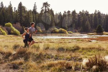 Man and woman running in nature near a lake, side view