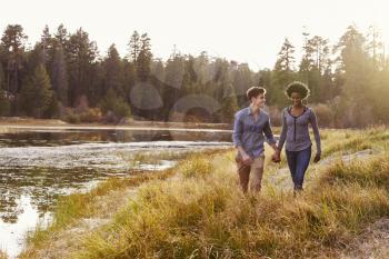 Mixed race couple holding hands, walking near a rural lake