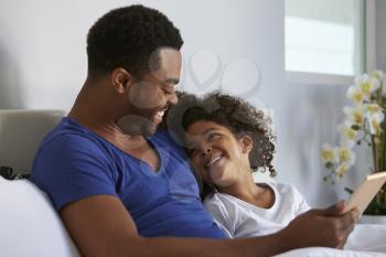 Black father and daughter relaxing in bed look at each other