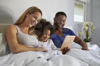 Mixed race couple and young daughter laugh in bed together