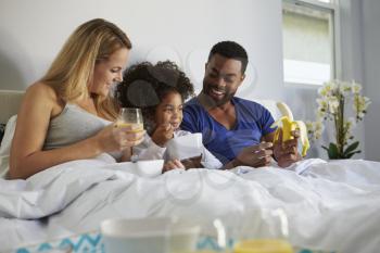 Mixed race couple and young daughter eating in bed together