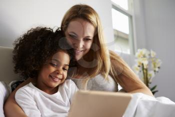 Caucasian mum and black daughter use tablet in bed, close-up