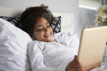 Smiling young girl lies in bed uses digital tablet, close up