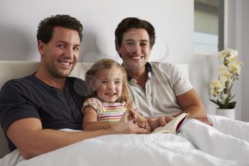Young girl in bed with her male parents, looking to camera
