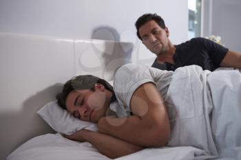 Man sitting up in bed, looking while his boyfriend sleeps