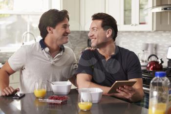 Male gay couple in kitchen with tablet looking at each other