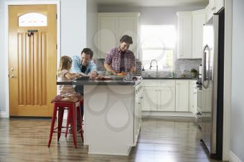 Male couple preparing a meal talk to their daughter in kitchen