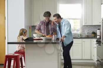 Daughter sits in kitchen while her male parents prepare meal