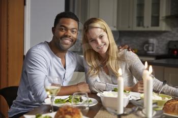 Romantic mixed race couple look to camera at meal in kitchen
