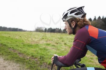 Male cyclist leaning on bike in open countryside, close up