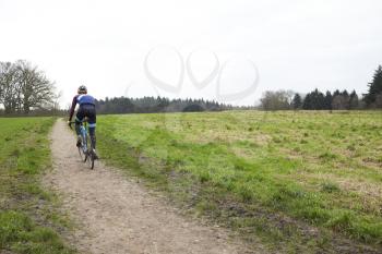 Cross-country cyclist on a path in countryside, back view