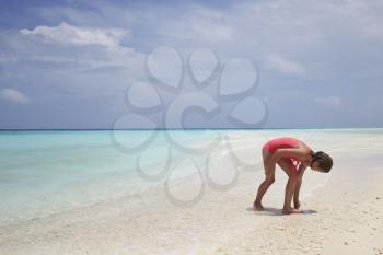 Young girl collecting sea shells on a white sand beach