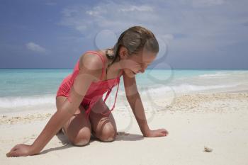 Kneeling girl looking at a tiny crab on a white sand beach