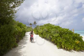 Back view of woman and girl riding bike on a path by a beach