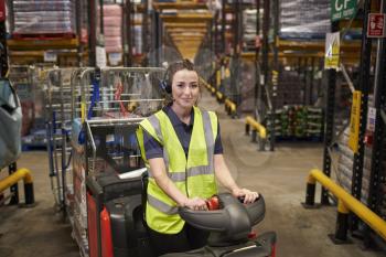 Young woman operating tow tractor in distribution warehouse