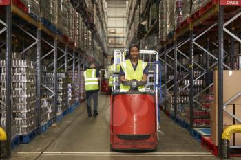 Woman operating tow tractor in a busy distribution warehouse