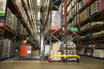 Man using aisle truck in a distribution warehouse, back view