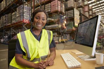 Woman with headset in a warehouse office looks to camera