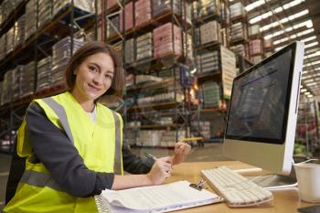 Woman working in the office of a warehouse looks to camera